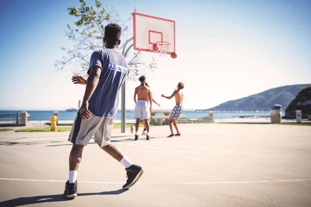 People playing basketball on an outdoor court with a scenic view at Avila Beach.