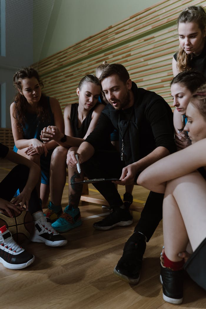 Basketball coach discusses strategy with female team indoors, focusing on teamwork and game planning.